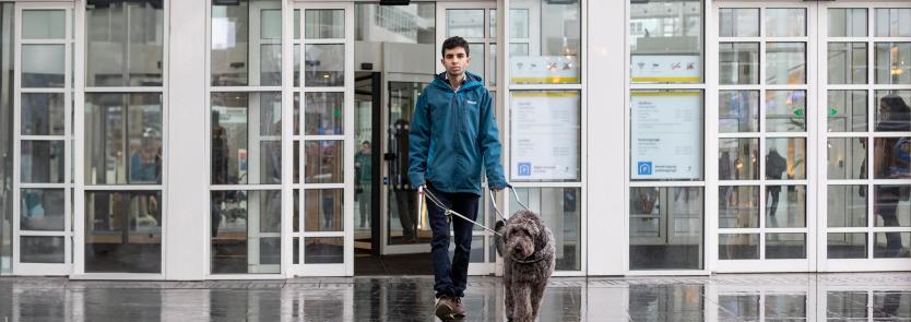 Man loopt met blindengeleidehond het stadhuis uit.
